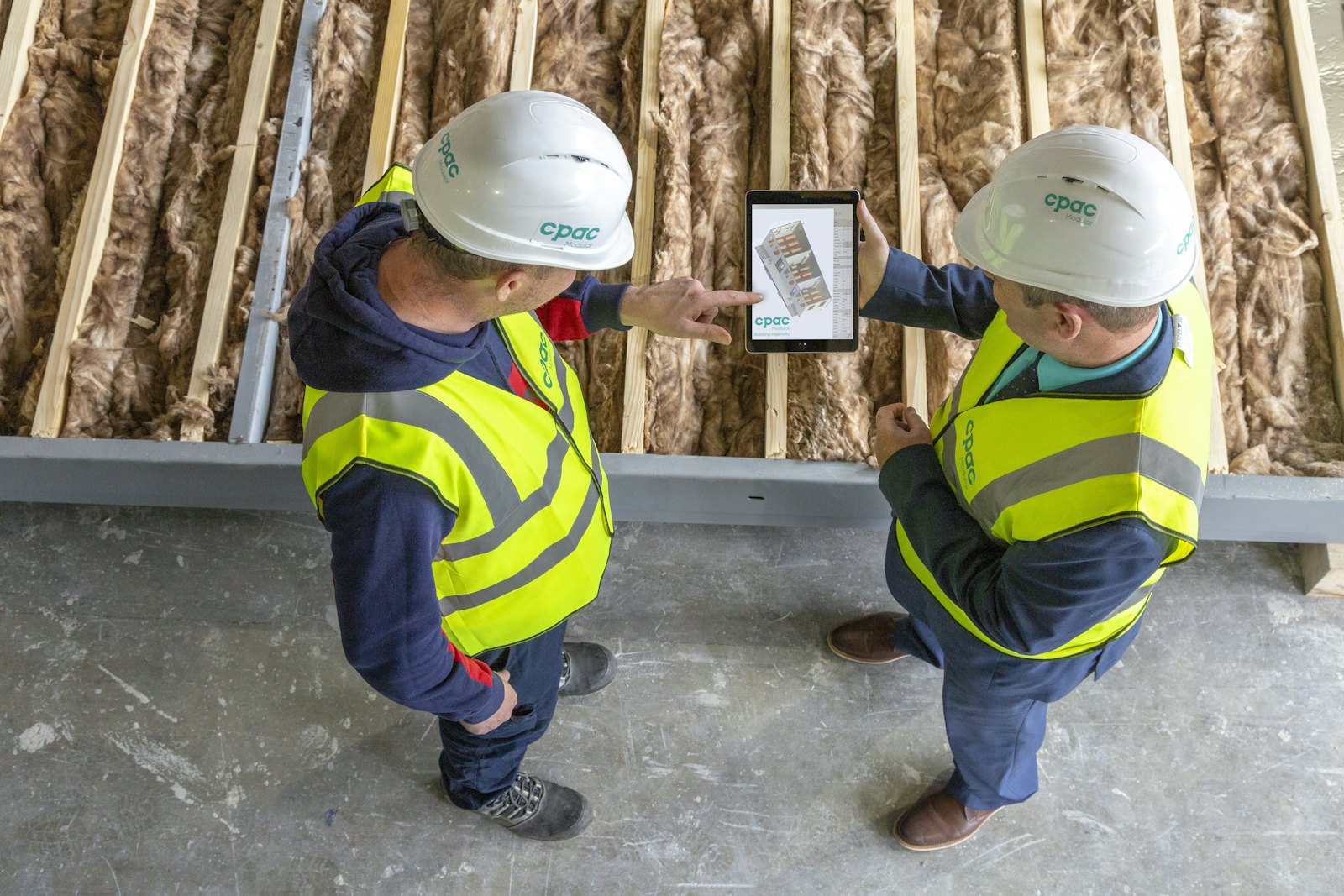 Two construction workers in hard hats and hi-vis vests reviewing plans on a tablet