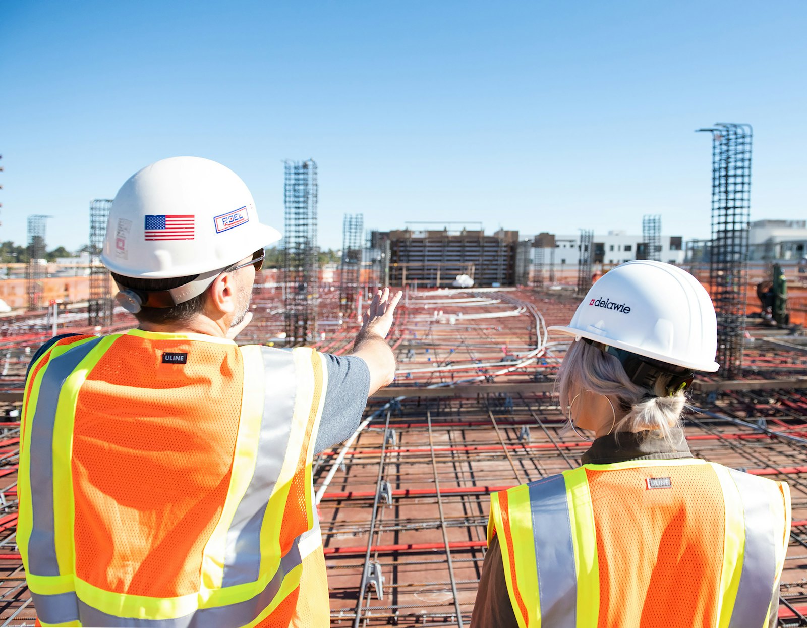 Two construction workers in safety vests and hard hats talking on a building site
