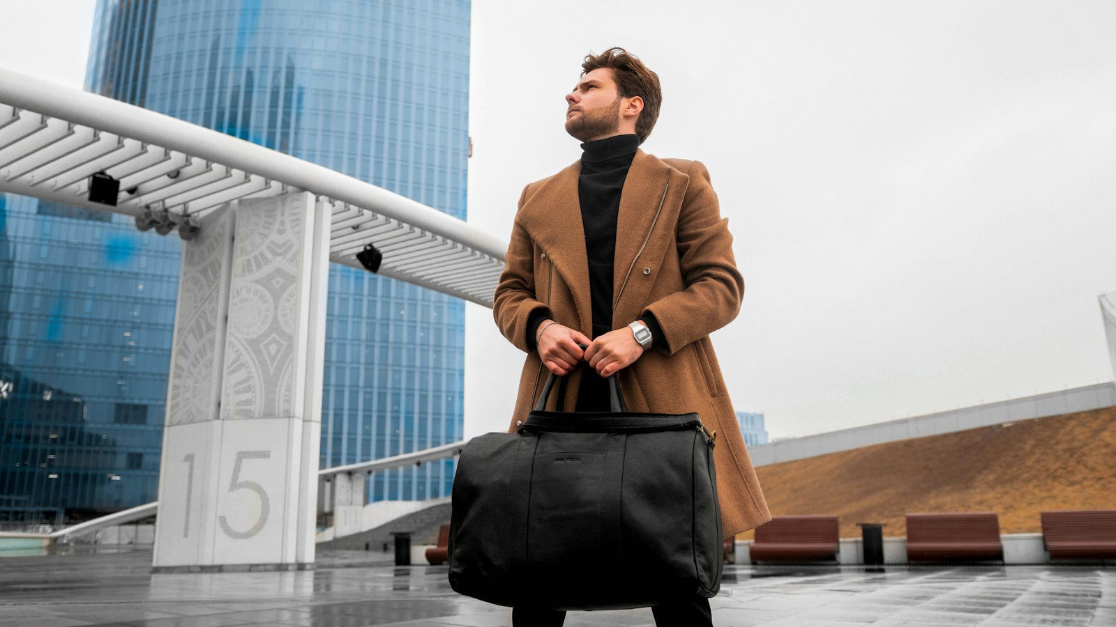 A man in a smart overcoat holding a briefcase beside a glass office building