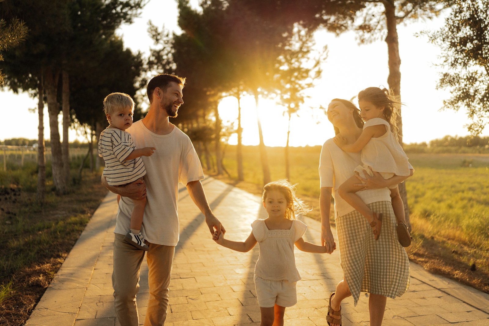 Parents and children walking hand in hand along a tree-lined path at sunset