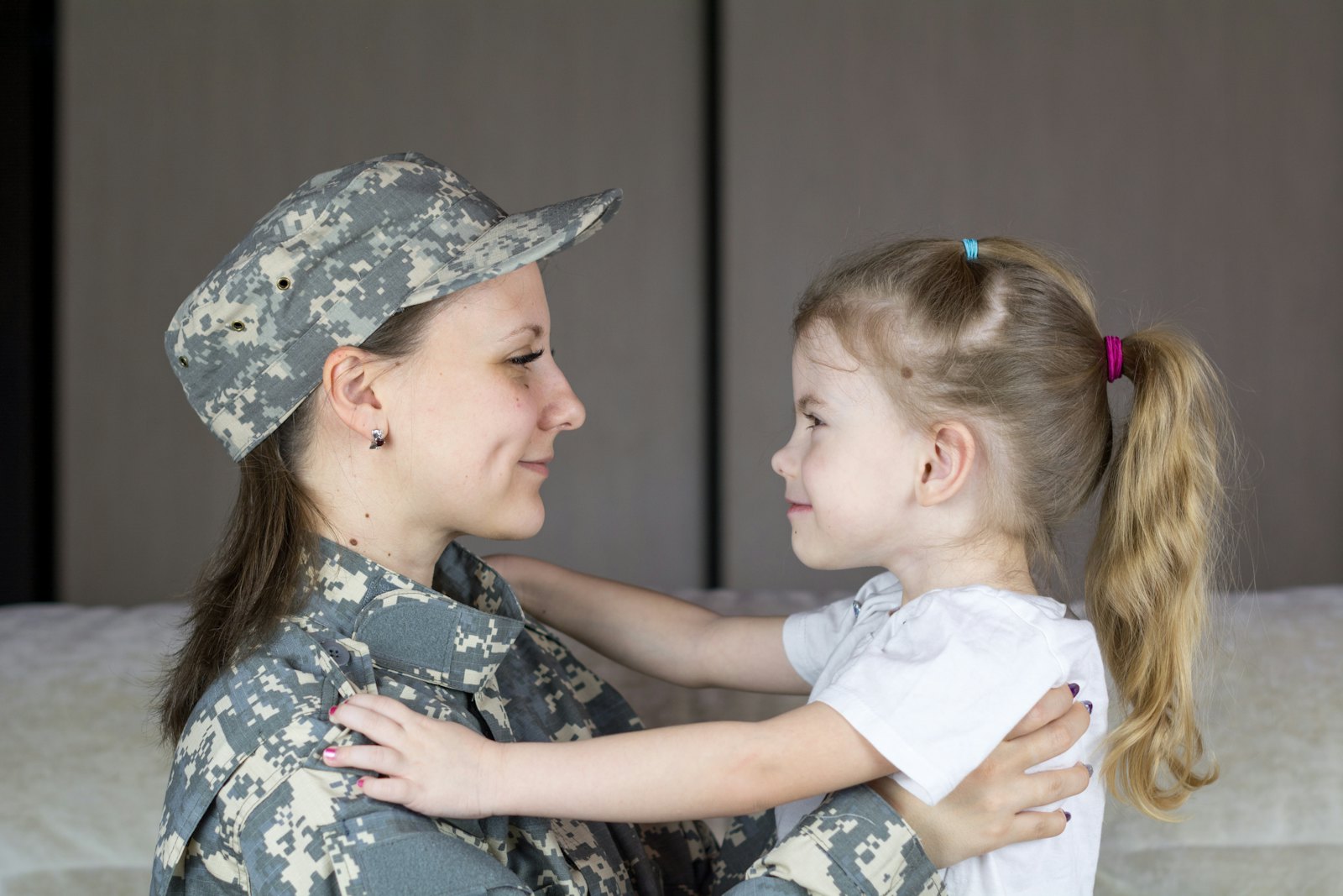 A parent in military uniform hugging their young daughter