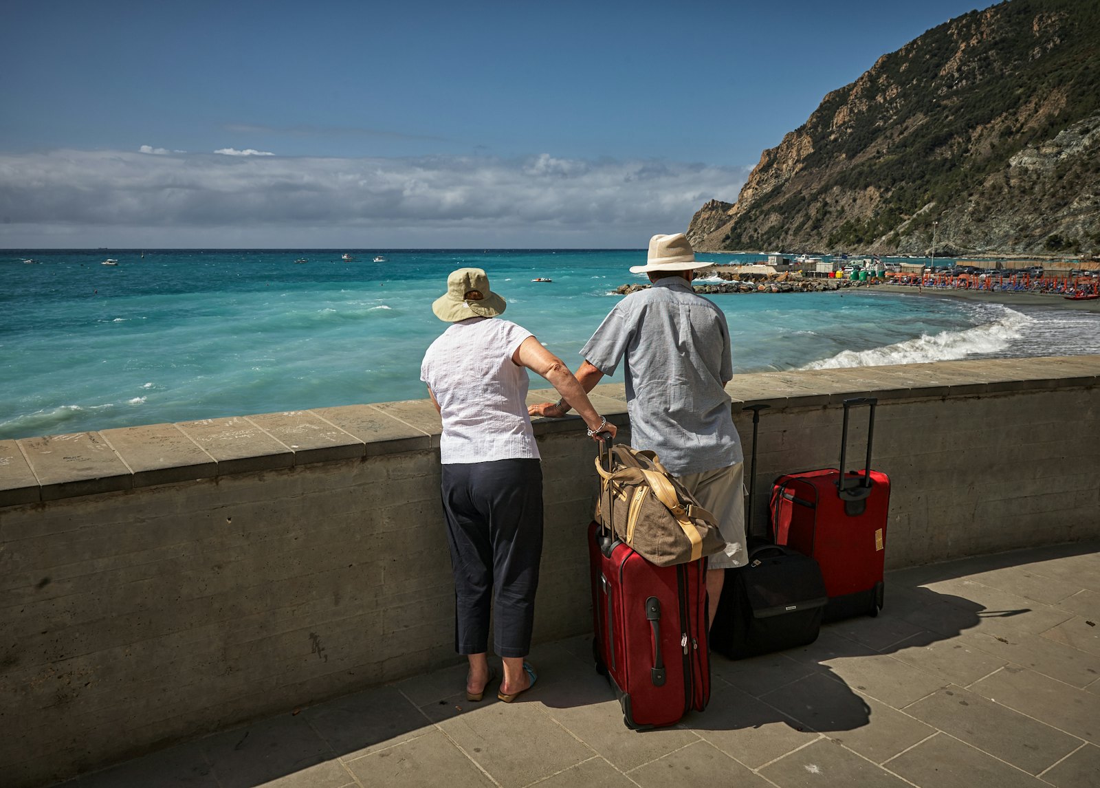 Two travellers with suitcases looking out over a seafront wall