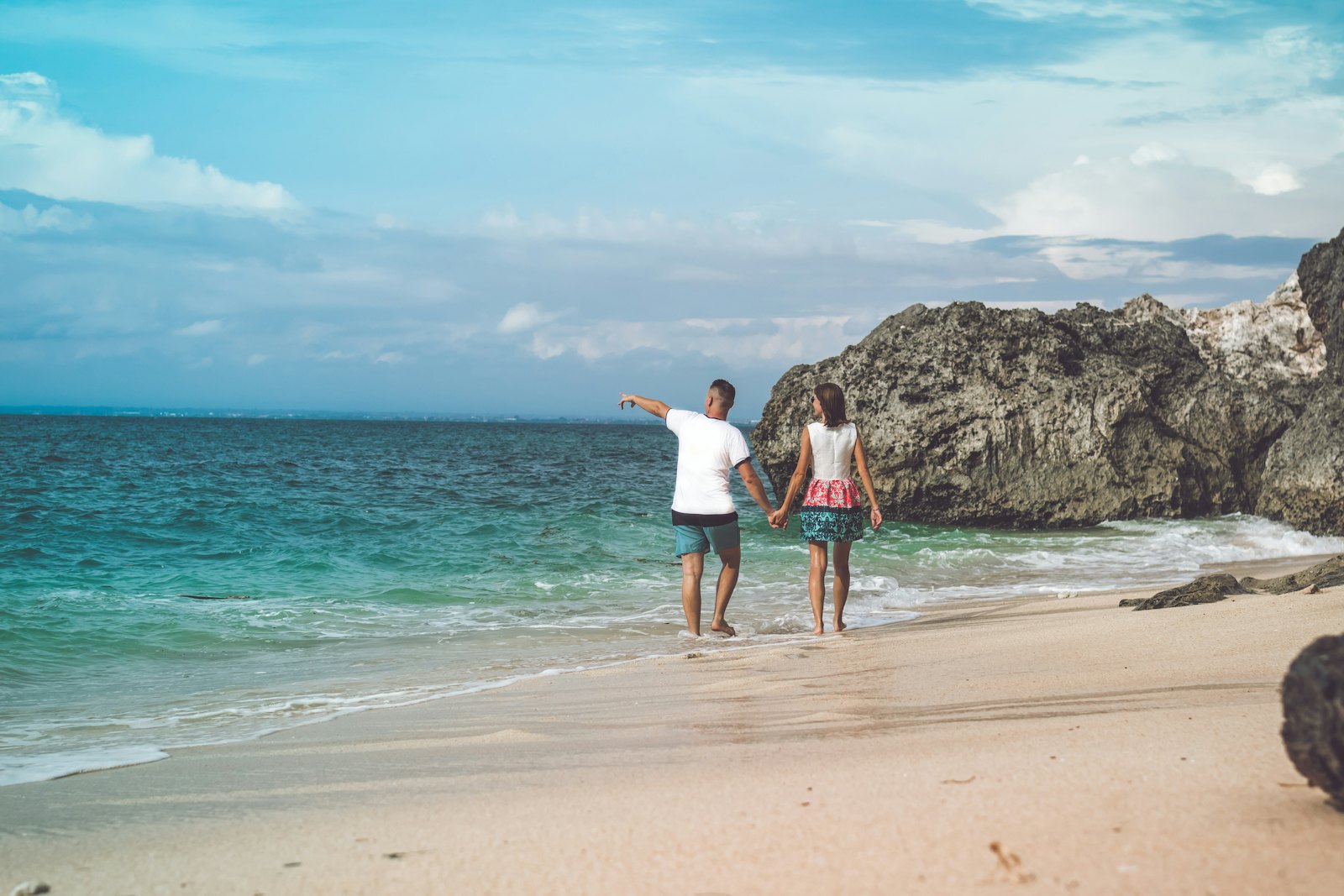 A couple walking hand in hand along a sandy beach beside rocky headlands