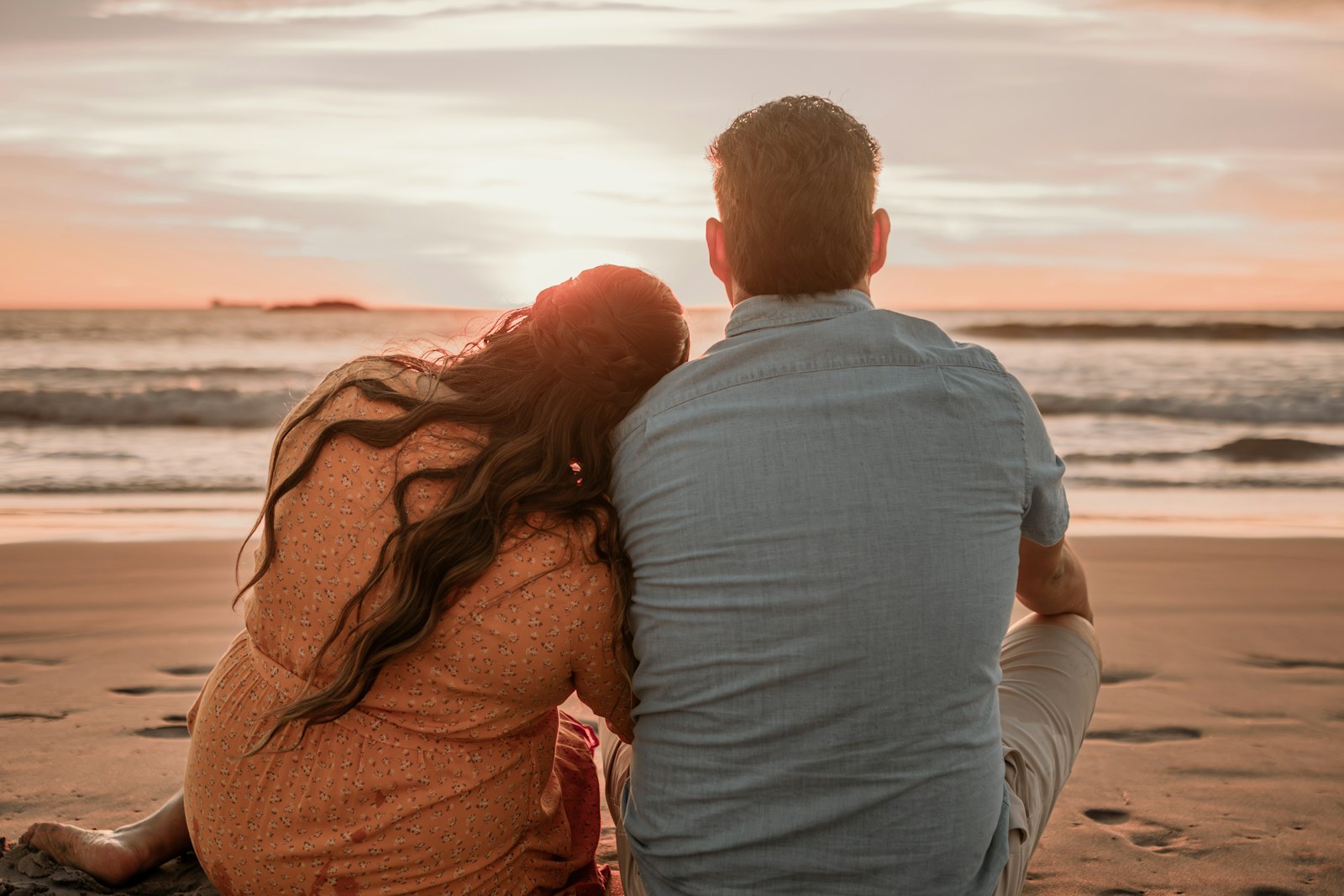 A couple sitting on a beach watching the sun set over the sea