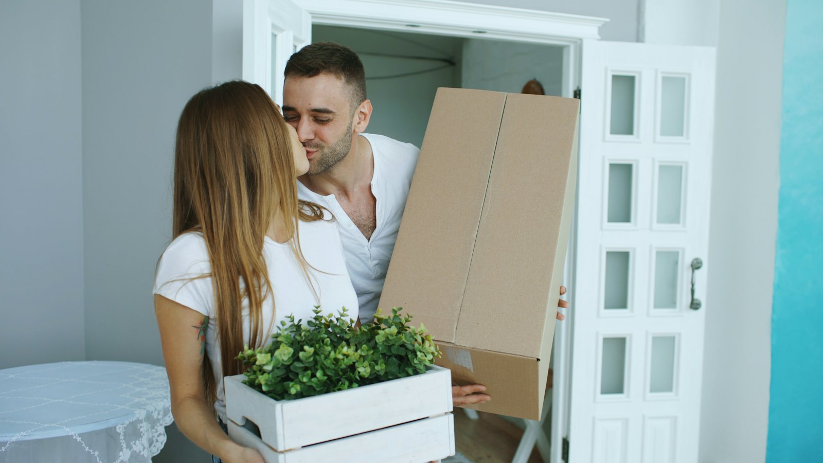 A couple carrying cardboard boxes through a doorway on moving day